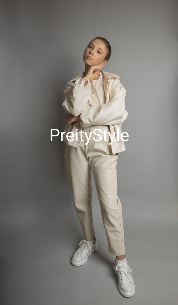 A model posing in a monochrome off-white smart casual outfit with white sneakers against a grey background.
