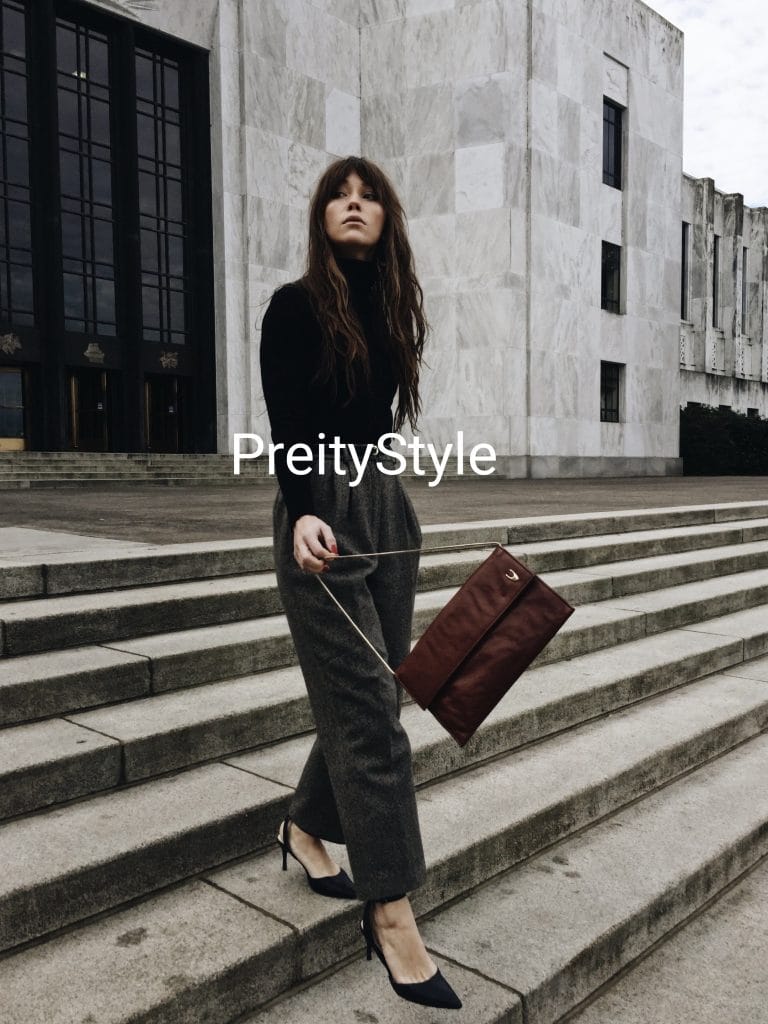 A chic woman wearing a fitted black turtleneck tucked into high-waisted grey trousers with a belt, illustrating the rule of thirds in outfit proportions.