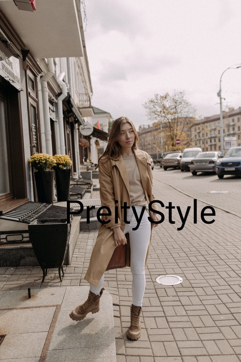 A young woman posing on a city sidewalk wearing a classic beige trench coat with white jeans and brown leather boots, illustrating everyday outerwear styling formulas.
